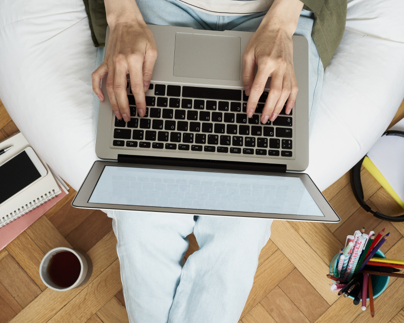 Person sitting down on white bean bag chair typing on a laptop